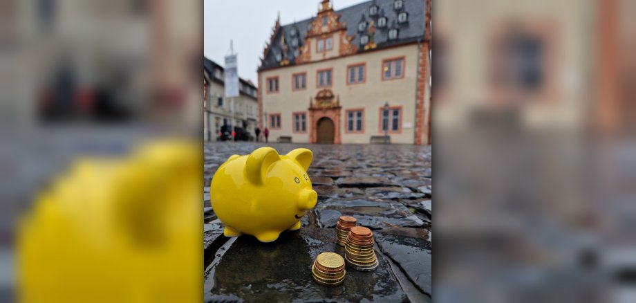 Sparschwein mit Kleingeld vor Rathaus